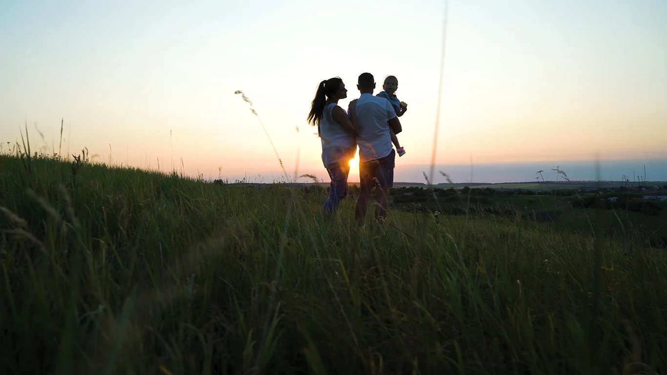 Pregnant couple with toddler daughter have leisure time outdoors at sunset.